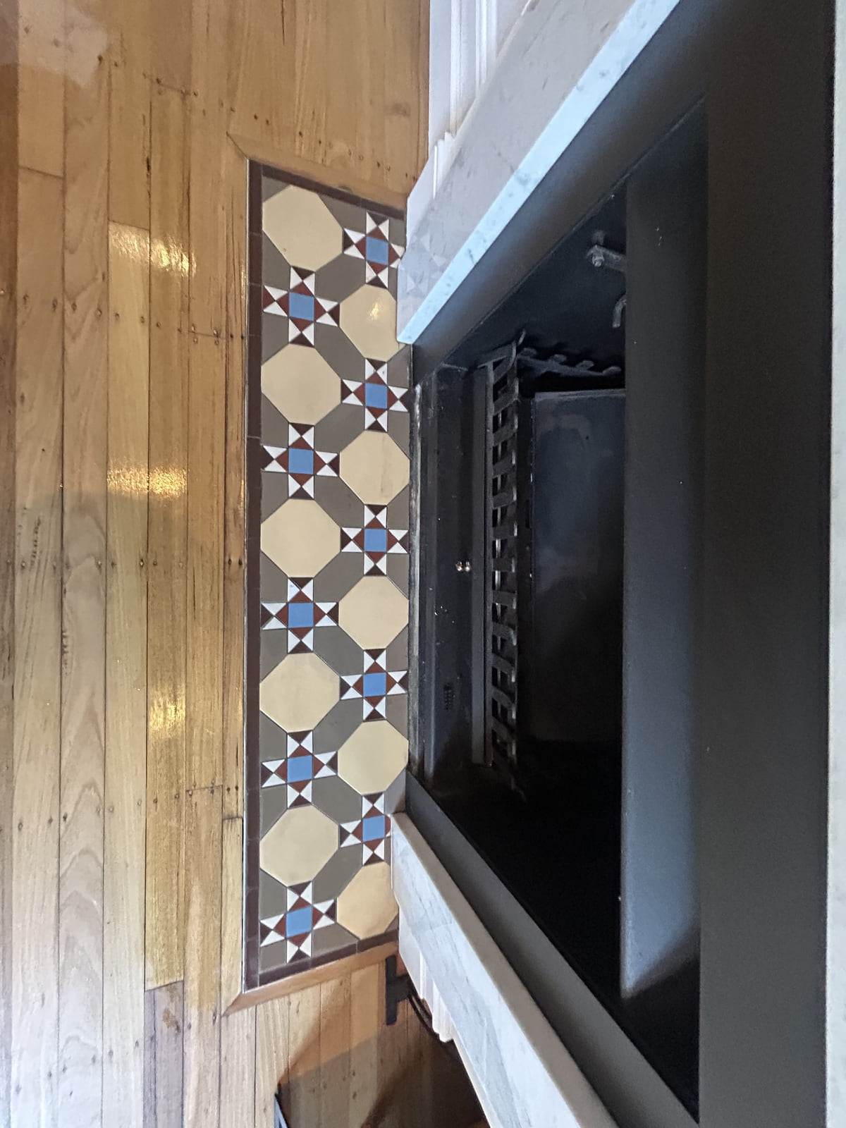 Geelong pattern hearth in cream, grey, light blue and brick red on a timber floor before a black fireplace, Annandale