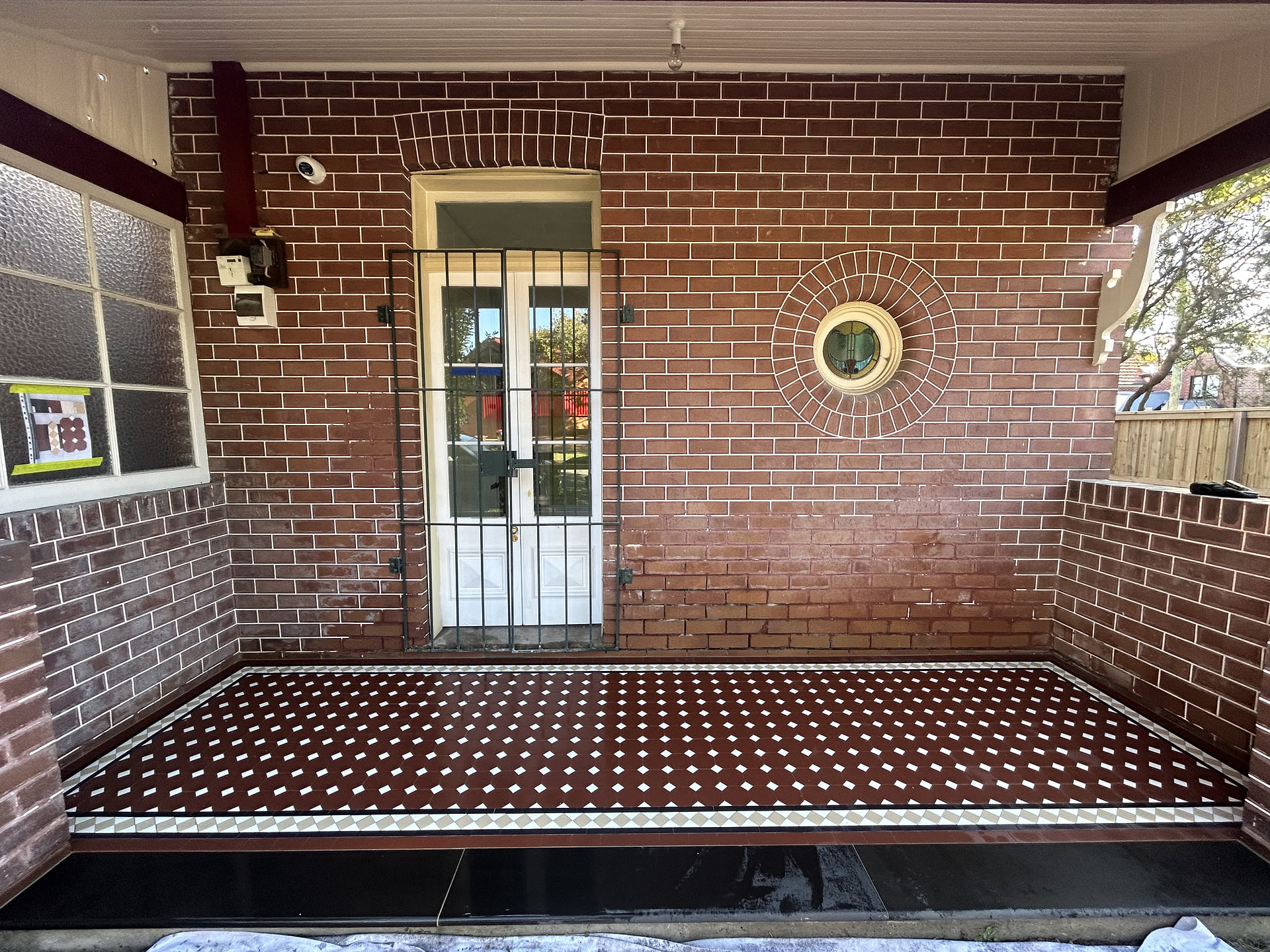 Front view of a red Octagon and Dot verandah on a brick house with a porthole window, Leichhardt